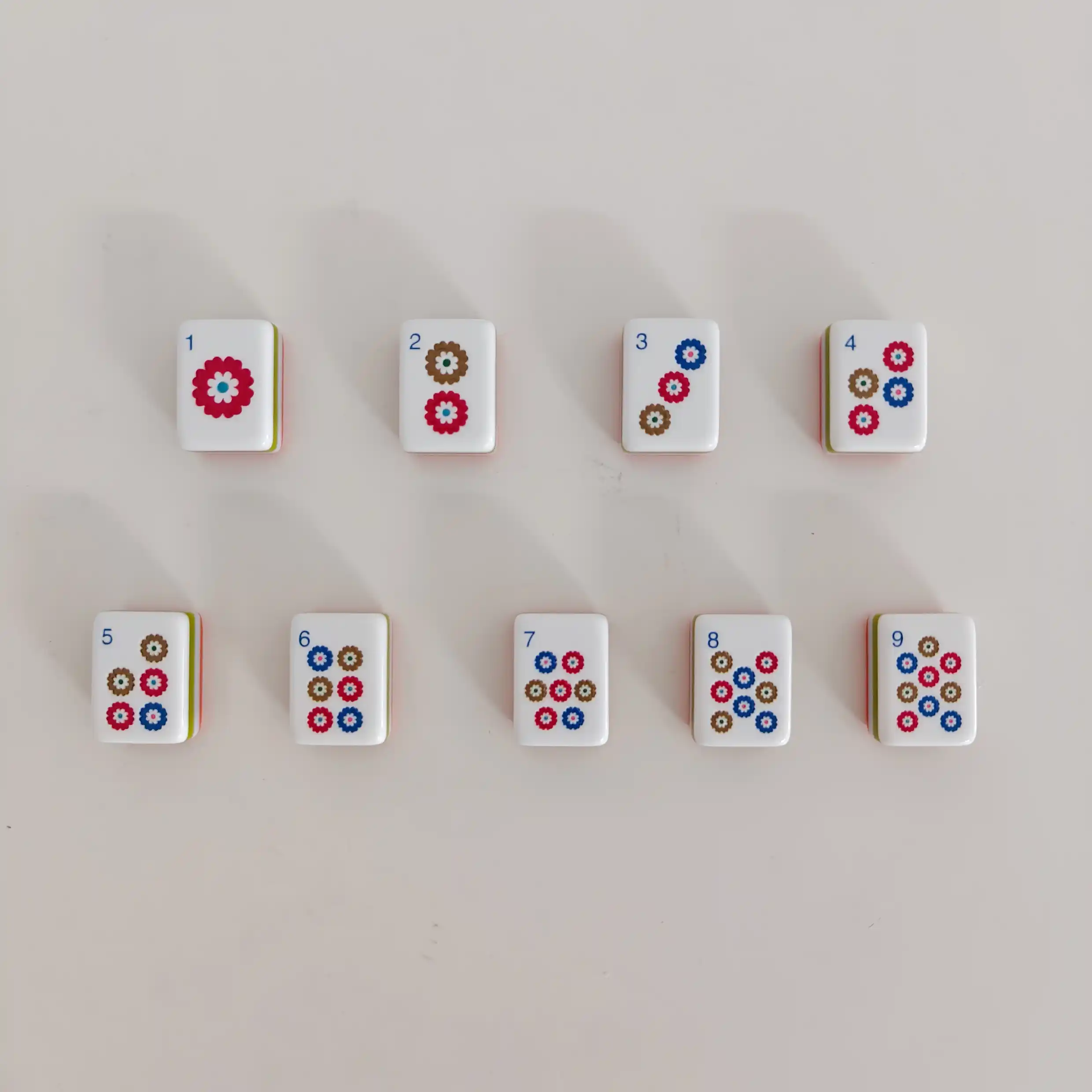 OMHJGO Cranes & Feathers mahjong Dot tiles 1 through 9 laid in two rows showing tricolor chrysanthemum daisy medallion patterns in crimson red cobalt blue and antique brown on white polished acrylic