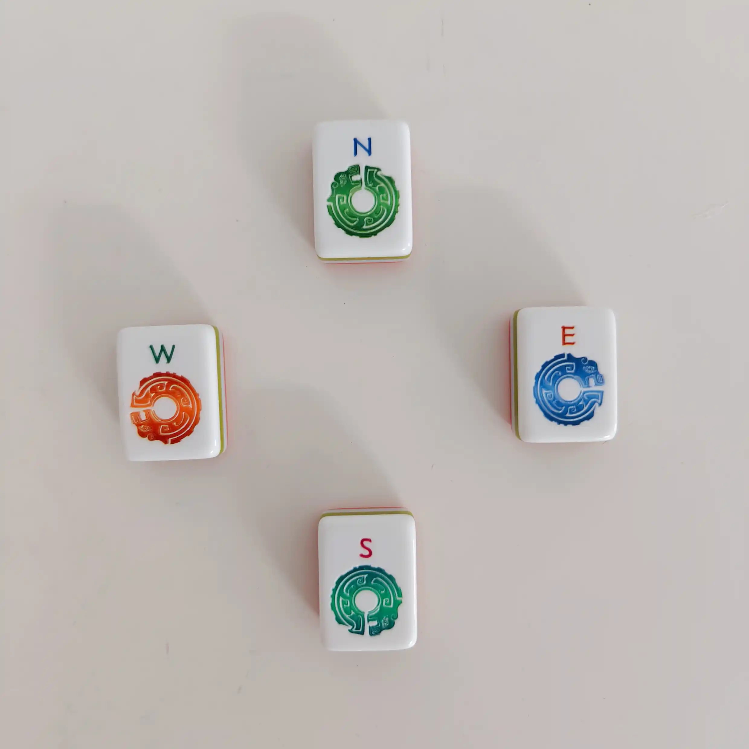 OMHJGO Cranes & Feathers four Wind tiles arranged in compass formation showing North green jade disc, East blue jade disc, West amber-rust jade disc, and South teal jade disc designs on white acrylic
